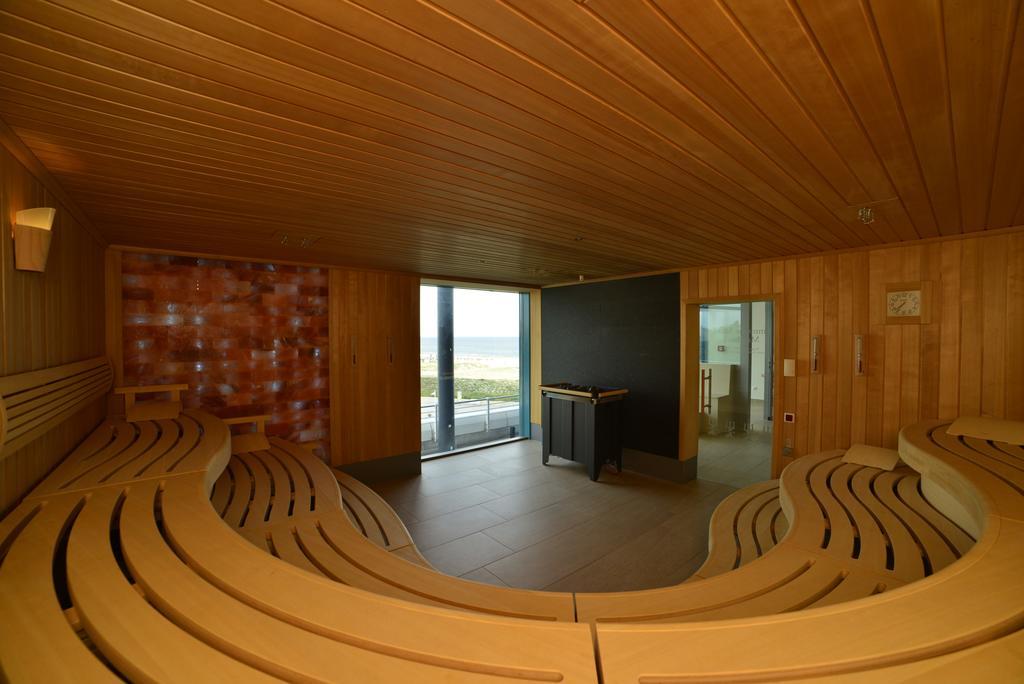 Hotel Neptun Rostock Eksteriør bilde The image depicts a modern sauna interior. The walls are made of wood, contributing to a warm and natural atmosphere. The seating is arranged in a curved design, allowing for multiple people to relax comfortably. Large windows provide a view of the o