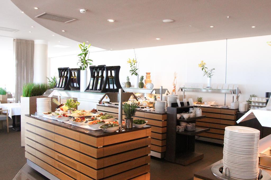 Hotel Neptun Rostock Eksteriør bilde The photo depicts a modern buffet setup in a bright, well-lit dining area. There are several wooden serving stations arranged neatly, each featuring a variety of food items. The buffet includes salads and other dishes, presented in an organized manne