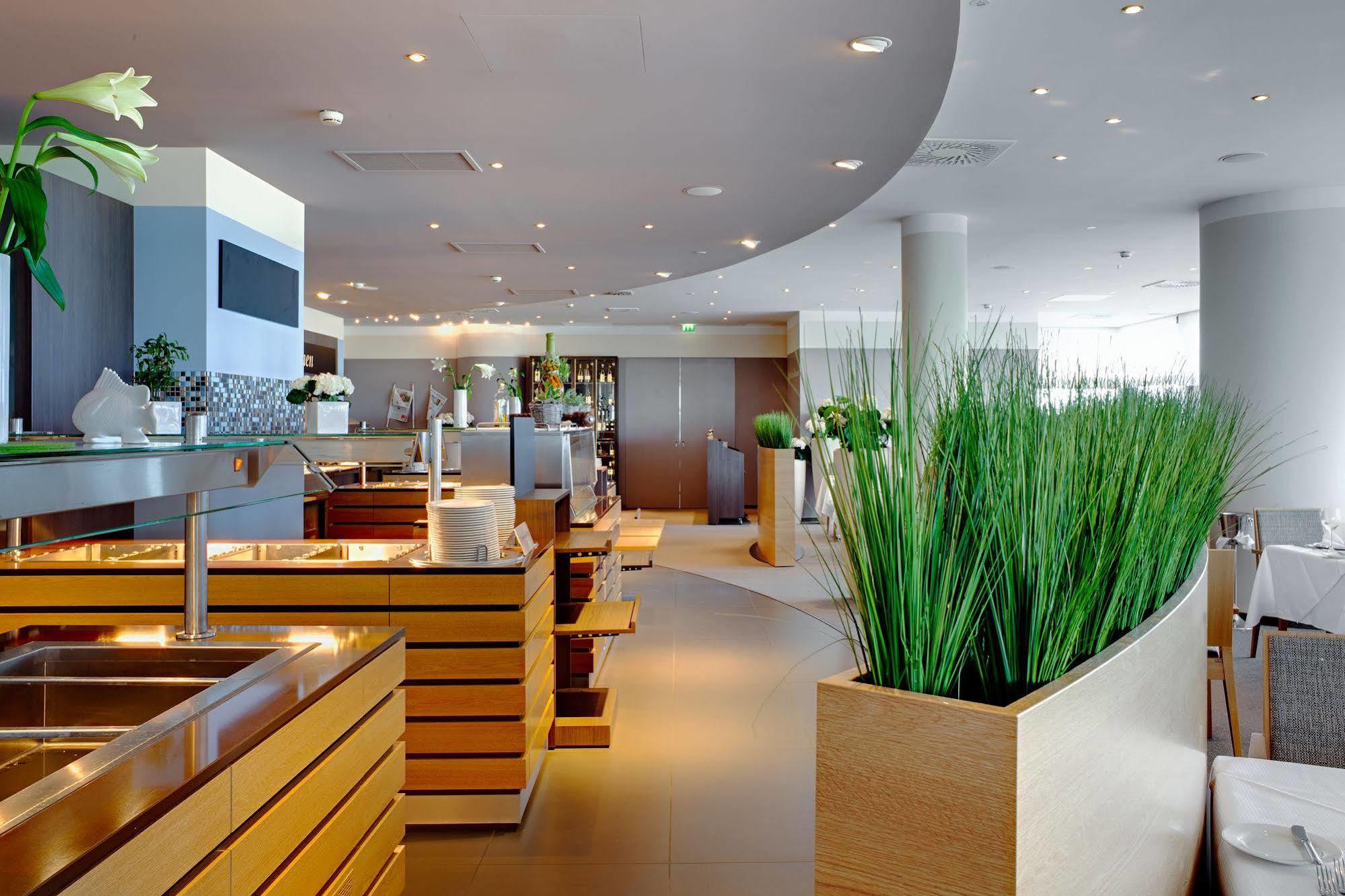 Hotel Neptun Rostock Eksteriør bilde The photo shows a modern restaurant interior featuring a sleek, contemporary design. The space includes wooden elements, likely part of the furnishings, with clean lines and a stylish layout. There are several dining areas, with wooden tables and ben