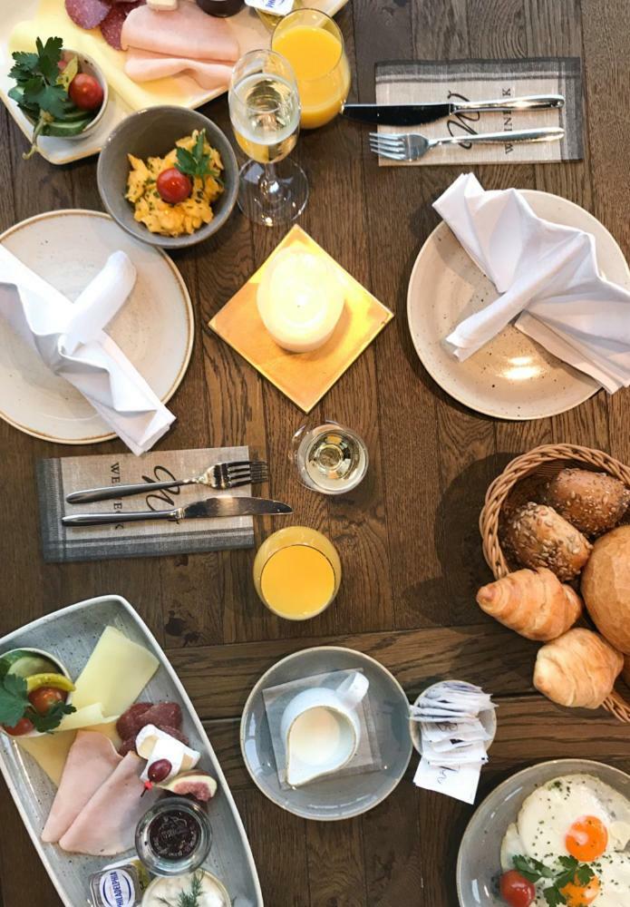 Hotel Neptun Rostock Eksteriør bilde The photo displays a dining setup featuring a wooden table with various food items. There are two plates set at the table, alongside white napkins elegantly folded. A small square plate with a lit candle sits in the center. To one side, there's a gla
