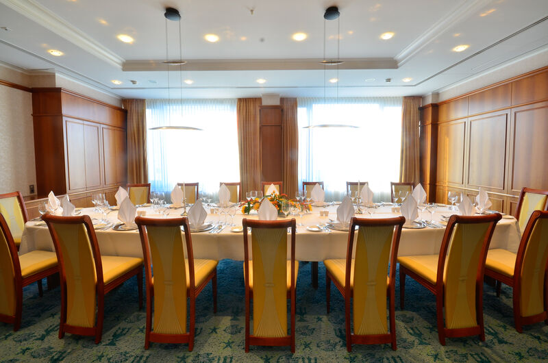 Hotel Neptun Rostock Eksteriør bilde The photo shows a beautifully arranged dining room. There is a long rectangular table set for a formal meal, with white tablecloths and neatly arranged place settings that include plates, cutlery, and folded napkins. The chairs around the table have 